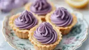 A close-up of mini lemon tarts with lilac-colored meringue swirls