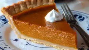 pumpkin pie with whipped cream on top sits on a white plate next to a fork
