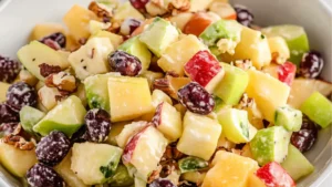 a glass bowl filled with fruit salad next to an image of apples, grapes and pecans