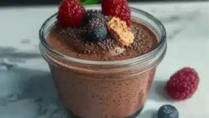 high protein chocolate chia pudding in a glass bowl with whipped cream and chocolate on top