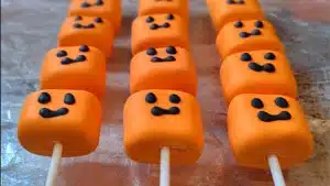 several rows of orange candy sticks with black icing on them
