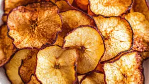 healthy air fryer apple chips - 2 ingredients only on a plate with apples in the background