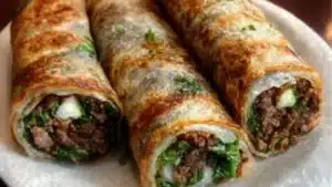 thai beef rolls on a white plate with sauce and garnishes in the background