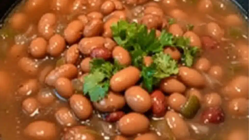 a close up of a bowl of food with beans and meat in it on a wooden table