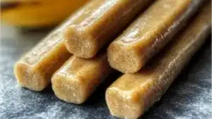 banana and peanut butter chew sticks for dogs on a table with nuts, bananas and peanuts in the background