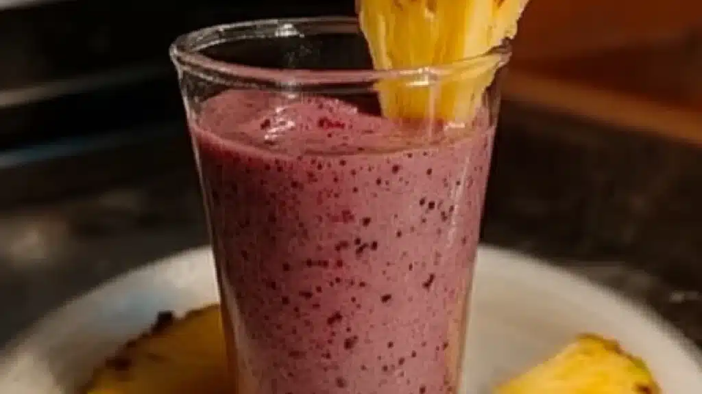 a smoothie with cranberry and pineapple is in a glass on the table