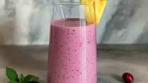 a smoothie with cranberry and pineapple is in a glass on the table