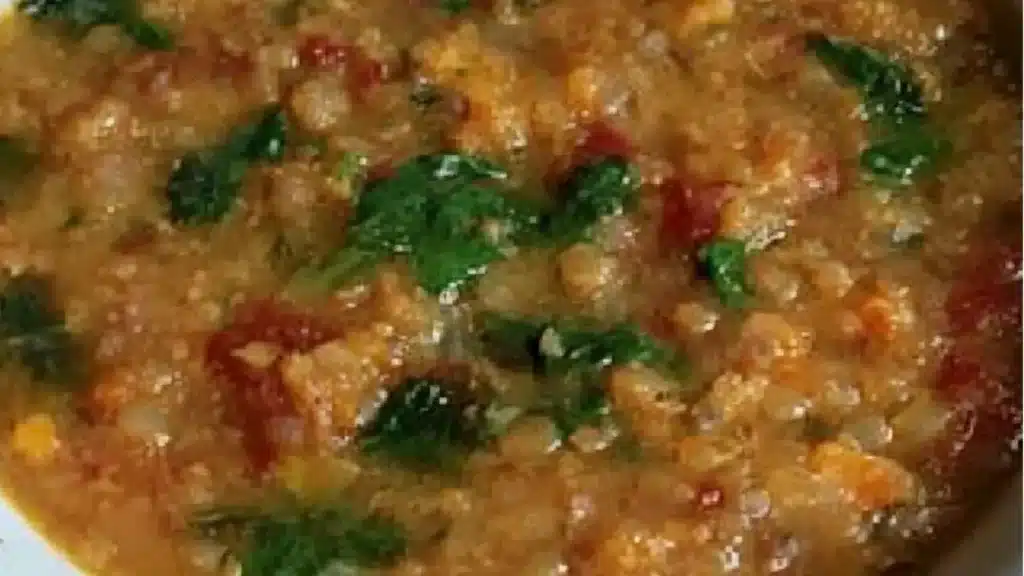 red lentil and spinach soup in a white bowl with a spoon on the side